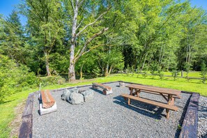 Un espace de pique-nique équipé de bancs et d’un foyer, le tout entouré d’arbres.