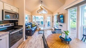 A modern kitchen with a built-in oven, microwave, and stainless steel appliances. There is a dining area with a wooden table and chairs, and a large window providing a view of the outdoors.