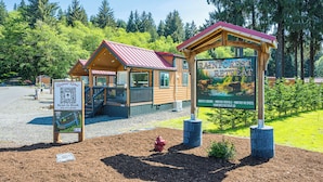 A cabin-style retreat with a red roof, a signboard advertising nightly lodging and monthly rentals, and a QR code for booking.