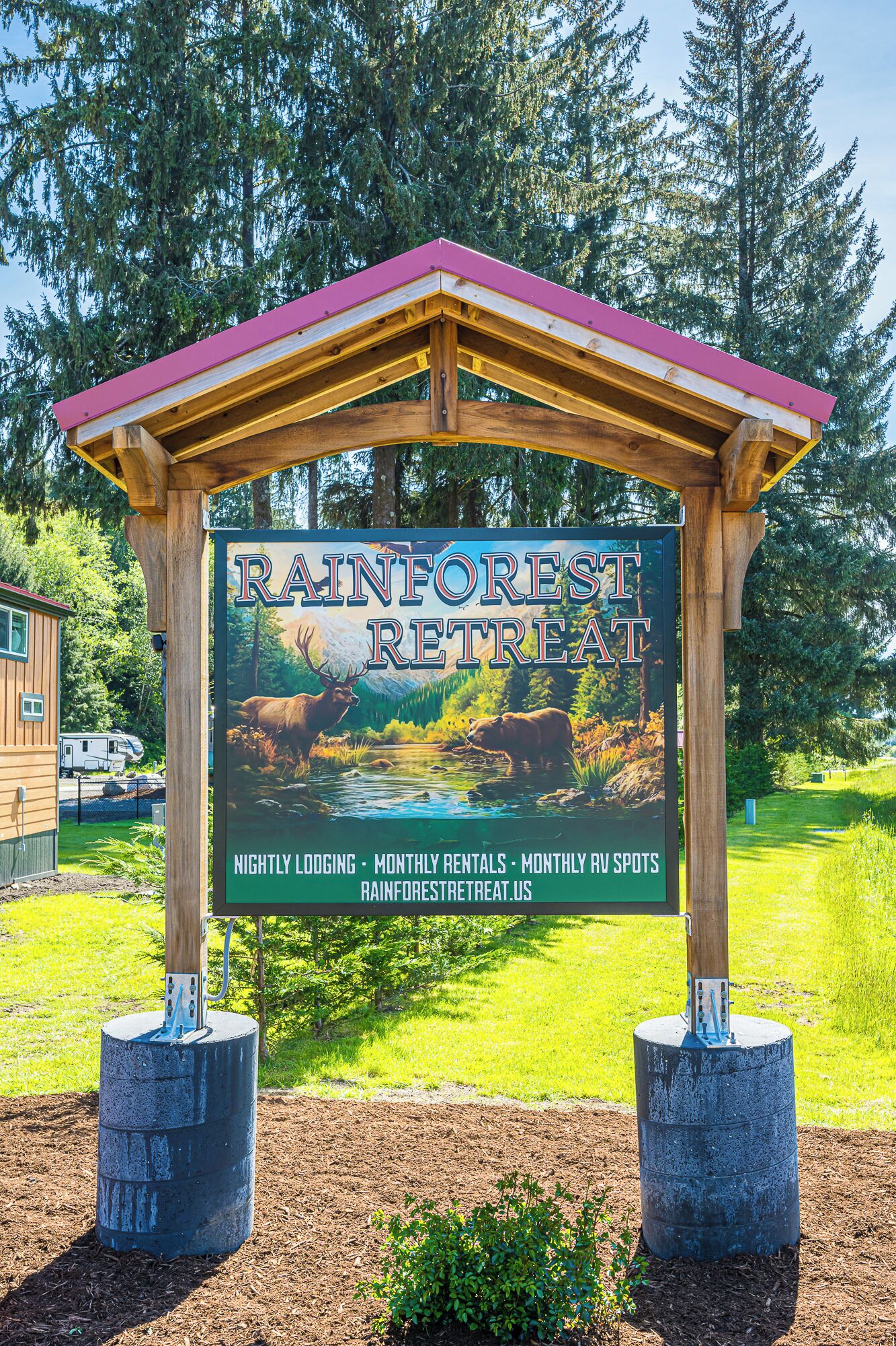 A wooden sign for Rainforest Retreat with a red roof, advertising nightly lodging, monthly rentals, and RV spots.