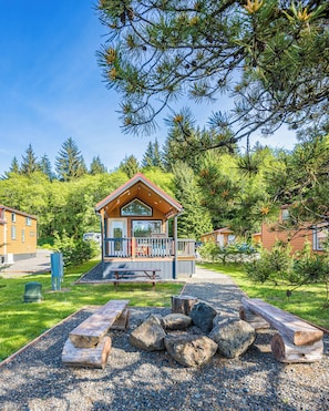 Une cabane dotée d’une terrasse, entourée d’arbres et bordée d’un chemin de gravier.