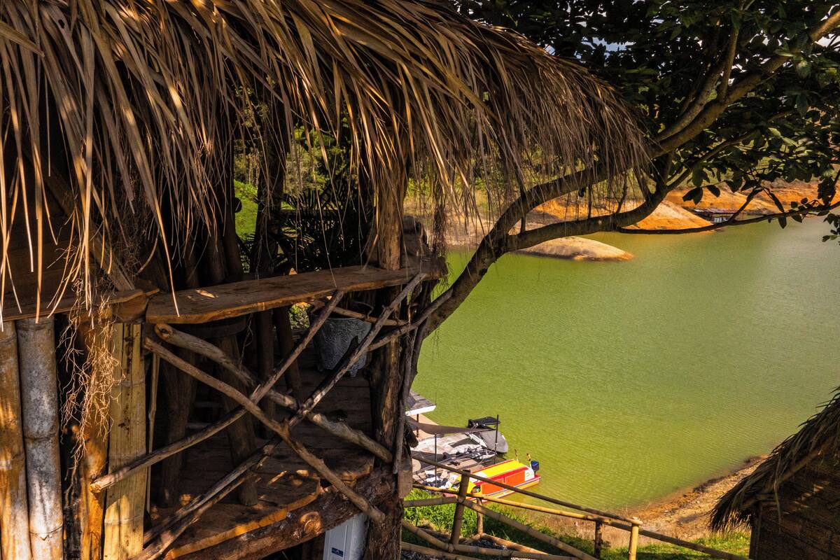 A thatched-roof structure with a wooden staircase leading to a platform overlooking a calm body of water.