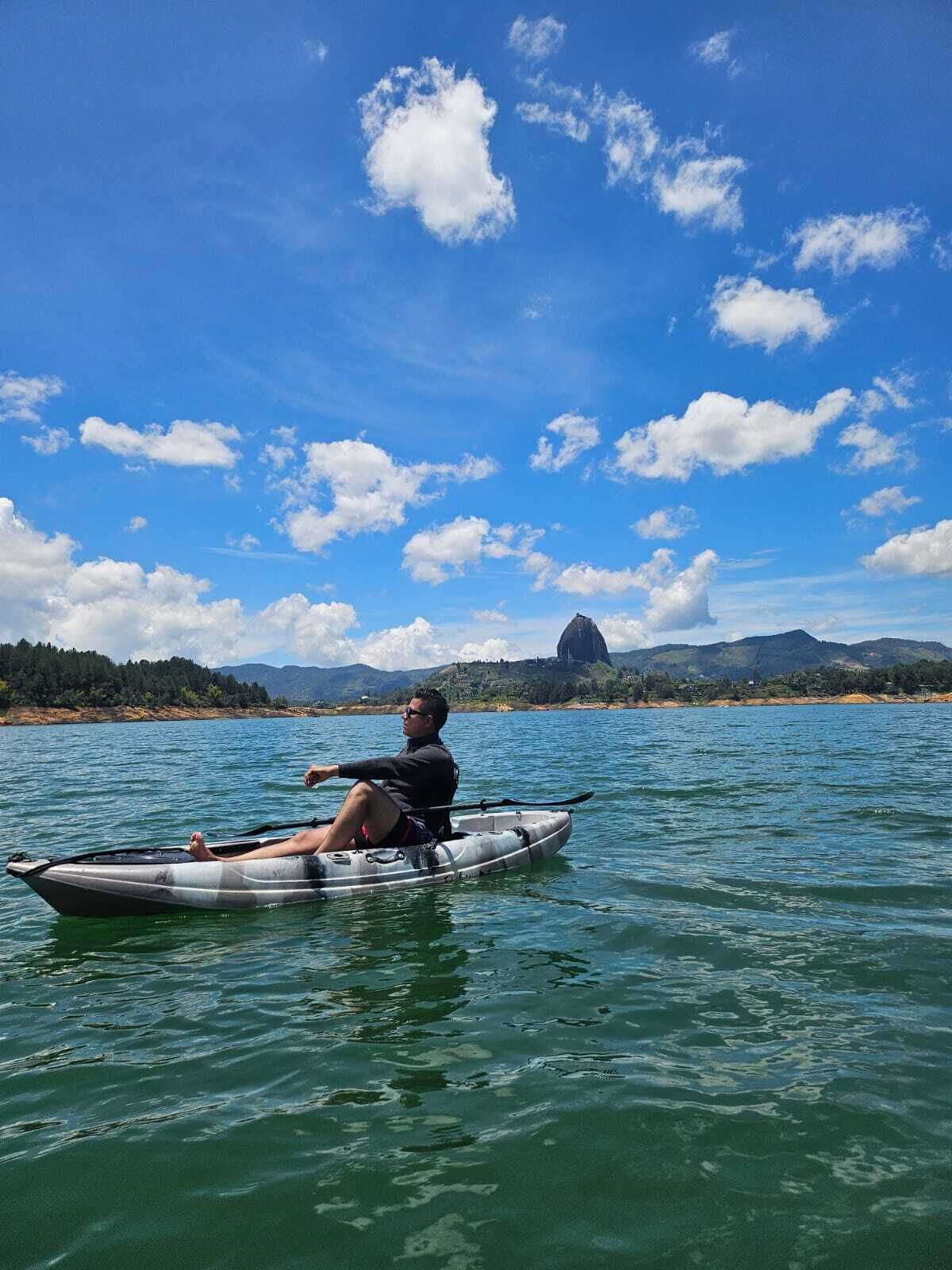 Una persona en un kayak sobre aguas tranquilas, con cielo despejado y montañas a lo lejos.