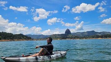 Una persona en un kayak sobre aguas tranquilas, con cielo despejado y montañas a lo lejos.