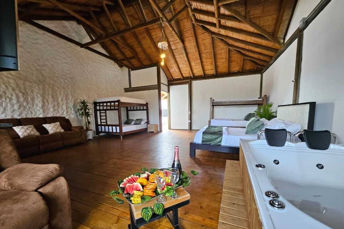A spacious room with a wooden floor, a hot tub, a sofa, and a dining table with fruit and a bottle.