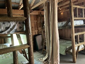 A rustic cabin interior with wooden bunk beds, a ladder, and a mesh screen door. - Summers Ranch Cabin (Clyde)