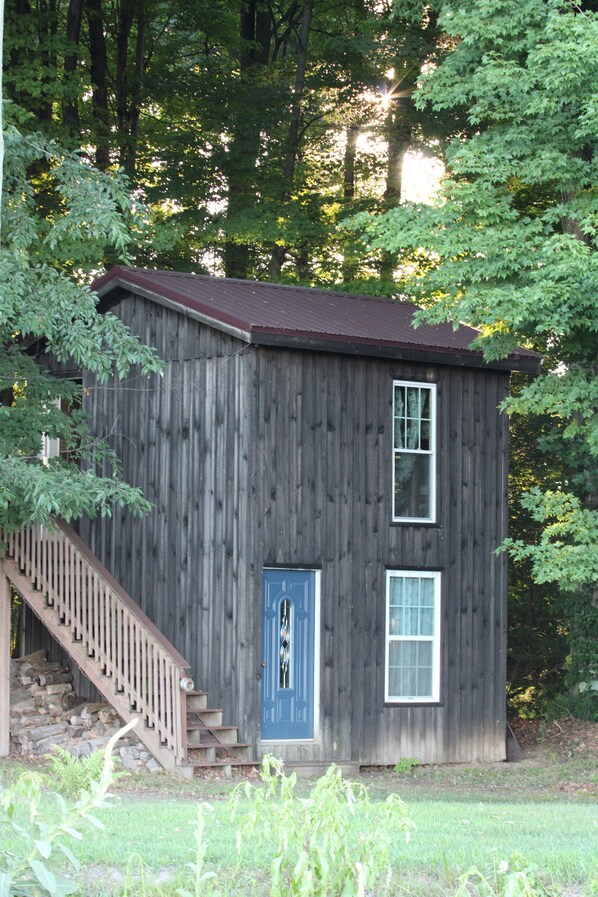 A wooden cabin with a blue door, a small window, and a staircase leading up to the entrance. - Summers Ranch Cabin (Clyde)