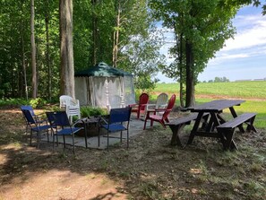 A picnic setup with a table and chairs, a covered seating area, and a view of a field. - Summers Ranch Cabin (Clyde)
