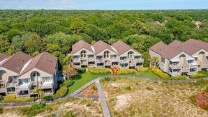 A row of modern, two-story cottages with balconies, surrounded by lush greenery and a clear sky. - Quaint Oceanfront, Pets ok, Pools, Golf, Amenity card! 1389 Pelican Watch (Seabrook Island)