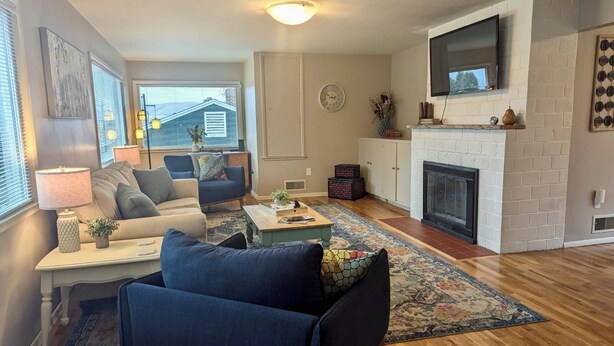 Ein Wohnzimmer mit Sofa, Sessel, Couchtisch, Kamin, Fernseher und Blick ins Freie.