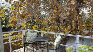 Eine Terrasse im Freien mit Tisch und Stühlen, umgeben von einem weißen Zaun, und ein Baum mit Herbstlaub im Hintergrund.