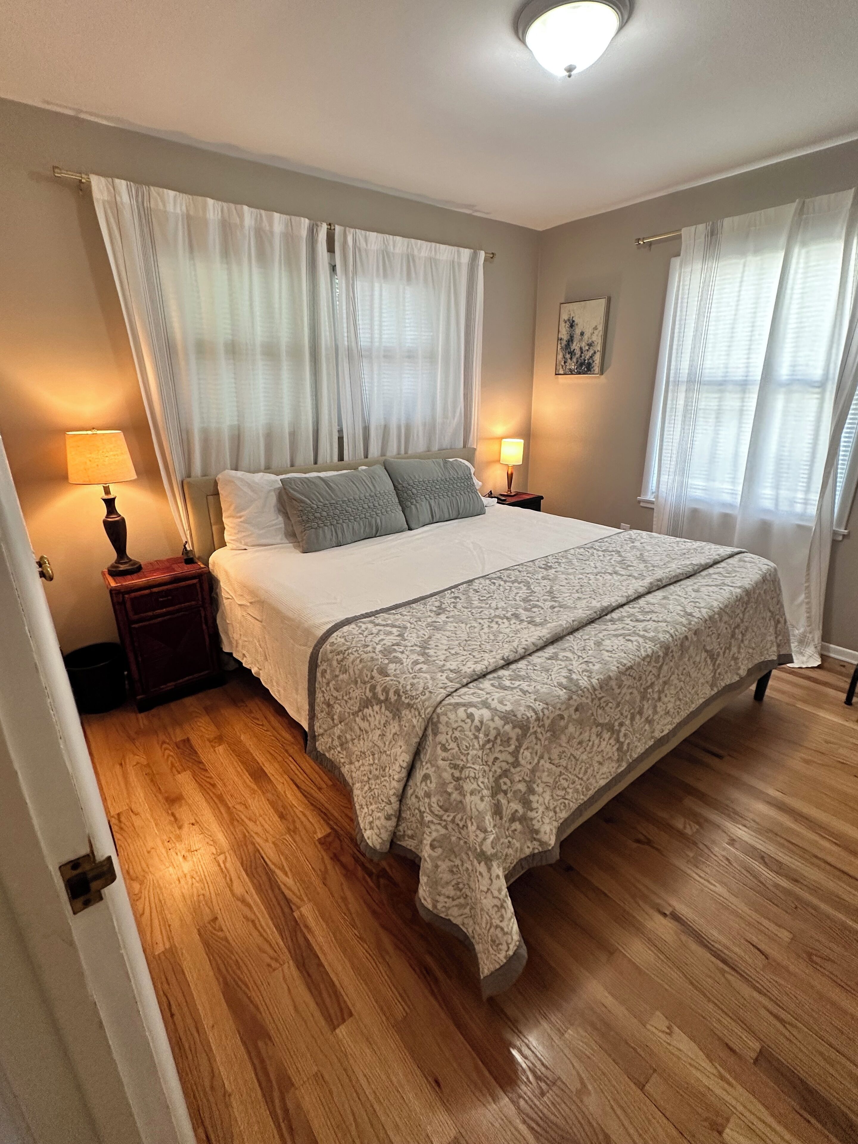 A bedroom with a large bed, two bedside lamps, a nightstand, and a ceiling light.