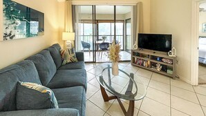 Ein Wohnzimmer mit einer Couch, einem Glastisch, einem Fernseher und einem Bücherregal.