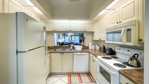 Eine Küche mit weißen Schränken, einem Kühlschrank, einer Mikrowelle, einem Herd und einem Fenster mit Blick nach draußen.
