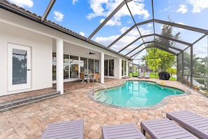 A covered outdoor swimming pool with a patio area, including lounge chairs and a table.