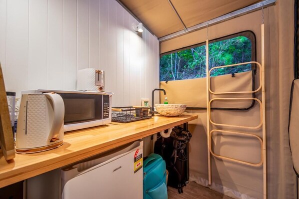 Una kitchenette compacta con microondas, hervidor y lavamanos pequeño.