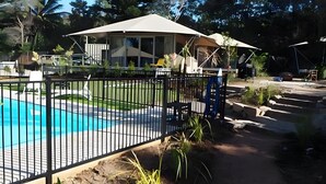 Una piscina con cerramiento metálico, un porche cubierto y una casa con un amplio ventanal.