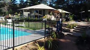 A swimming pool with a metal fence, a covered patio area, and a house with a large window.