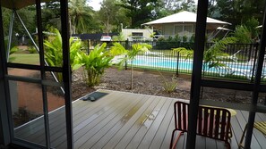 Una terraza de madera con piscina, rodeada por una valla y follaje.