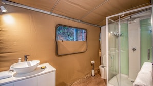 A compact bathroom with a white sink, a small window with a view of trees, a glass shower enclosure, and a towel on the floor. - Queen tent 10 Nelly bay (Nelly Bay)