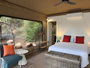 Habitación con carpa, cama, una mesita, sillas, vista al exterior y ventilador de techo.