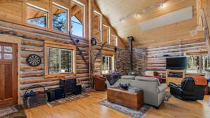 A log cabin interior with a fireplace, wooden floors, a television, and a cozy seating area. - Rustic and cozy log home, Room for the entire family.  (La Pine)