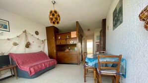 Una habitación con sofá, una mesa de comedor con sillas, un aparador de madera y una lámpara en el techo.