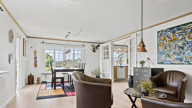 Un vaste espace de vie comprenant une table à manger, deux fauteuils en cuir, une table basse et un grand tableau abstrait.