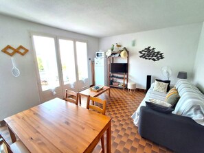 Ein kompakter Wohnraum mit einem Holztisch, einer Couch, einem Fernseher und einer Küchenzeile.