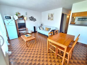 A compact living space with a kitchenette, a sofa, a dining table, and a patterned floor.