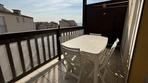 A balcony with a white table and chairs, a view of the city, and a dark wooden fence. - STUDIO MEZZANINE POUR 4 PERSONNES CLIMATISE (LE CAP D AGDE)