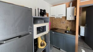 A compact kitchen with a refrigerator, microwave, coffee maker, and cabinets. - STUDIO MEZZANINE POUR 4 PERSONNES CLIMATISE (LE CAP D AGDE)