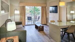 A modern hotel room with a glass dining table, a sofa, a TV, and a balcony with curtains.