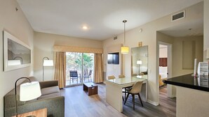 A modern hotel room with a living area, a dining table, and a kitchenette.