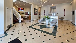 A spacious lobby with a geometric patterned floor, a chandelier, and a staircase leading to another area.