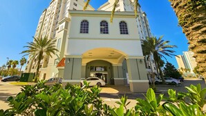 A multi-story hotel with a central entrance, surrounded by lush greenery and palm trees.