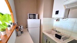 Eine kleine Küche mit Mikrowelle, Kühlschrank, Spüle und einem Fenster mit Pflanzen.