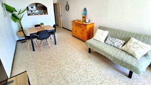 Ein gemütlicher Wohnbereich mit Essplatz, einer Couch mit gemusterten Kissen und einer kleinen Küchenzeile.
