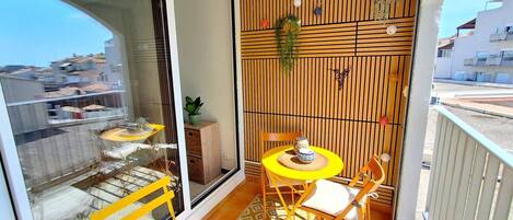 A balcony with a yellow table and chairs, a sliding glass door, and a view of the cityscape.