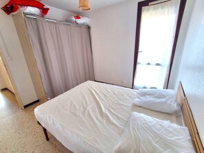 A bedroom with a bed, a window with curtains, and a door. - Appartement Climatise Proximité Plage et Commerces (LE CAP D AGDE)