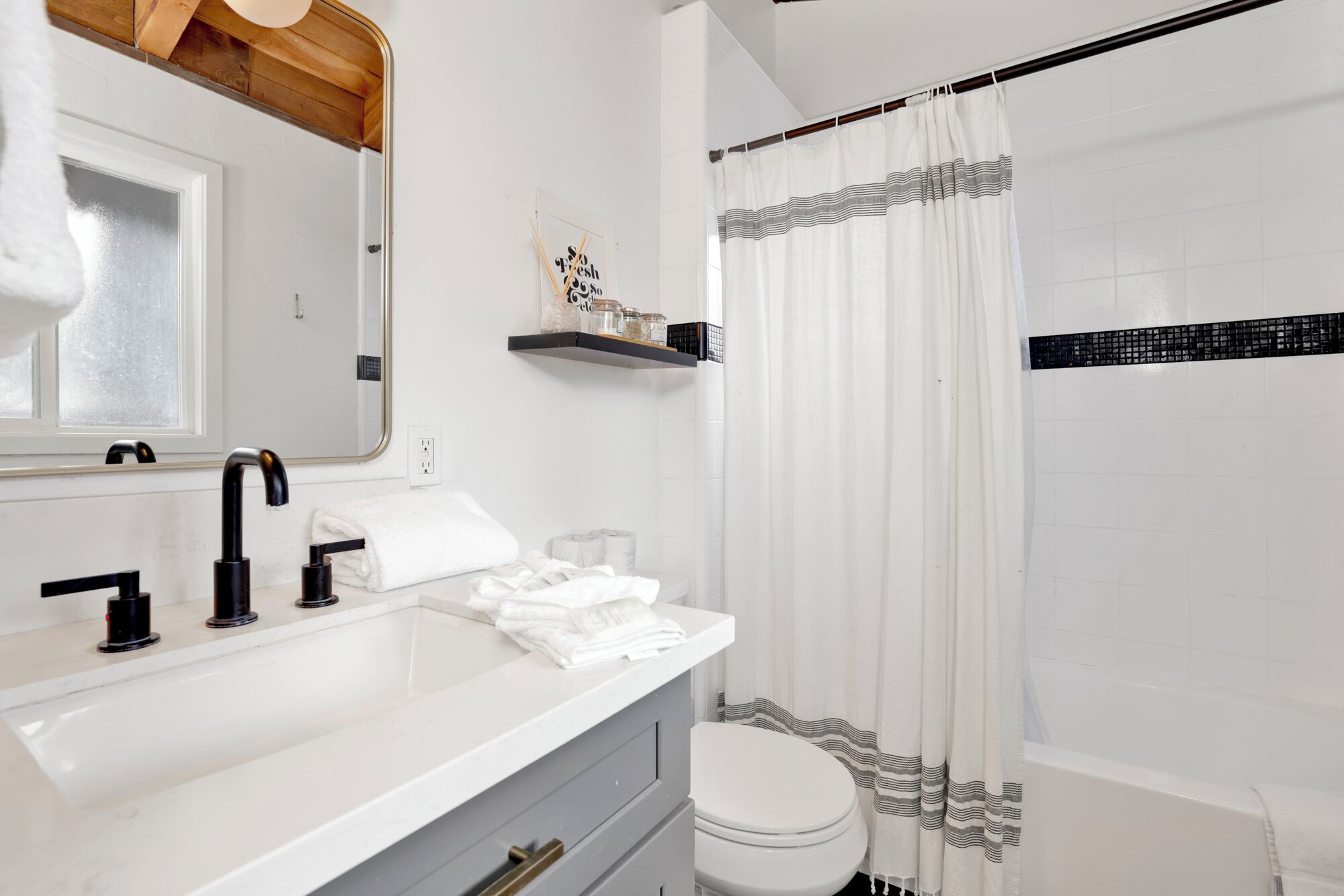 Un baño moderno con un lavamanos blanco, grifo negro y cortina de ducha a rayas.