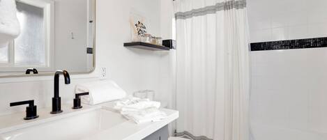 Un baño moderno con un lavamanos blanco, grifo negro y cortina de ducha a rayas.