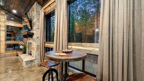 Un intérieur rustique avec une cheminée en pierre, des poutres en bois et une table ronde en bois sur laquelle est posé un saladier.