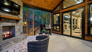 Un espace extérieur accueillant, avec des murs en pierre, une cheminée et une vue sur les arbres, visible à travers une porte vitrée.
