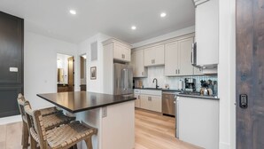 Una cucina moderna con mobili bianchi, elettrodomestici in acciaio inossidabile e un'isola in legno con sgabelli da bar.