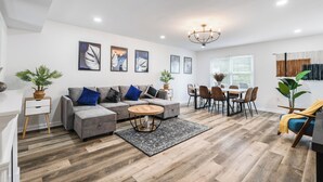 A modern living room with a grey sectional sofa, a round coffee table, and a dining area with a table and chairs. - 8-Person HotTub, Family&Group Friendly, EV Charger, Free Platinum Pool Pass (Mc Gaheysville)