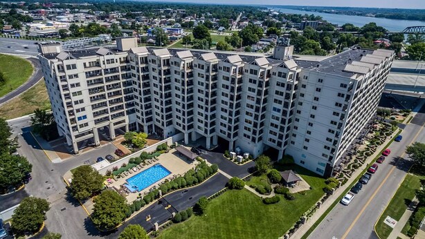 A multi-story hotel with a swimming pool, parking area, and a view of a river and bridge in the background. - BEST view of Louisville (Jeffersonville)