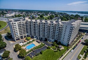A multi-story hotel with a swimming pool, parking area, and a view of a river and bridge in the background. - BEST view of Louisville (Jeffersonville)