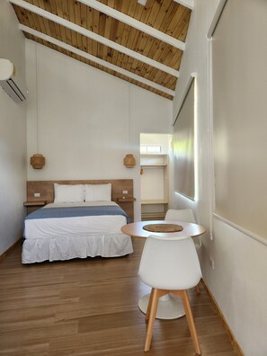 A bedroom with a bed, bedside tables, a round table with a chair, and a window. - Hermoso Estudio Cerca de la Playa ! (Uvita)