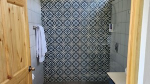 A bathroom with a wooden door, a patterned tile wall, a white toilet, and a blue cabinet.